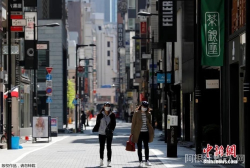 日本东京，戴口罩的女士走过空无一人的购物区。